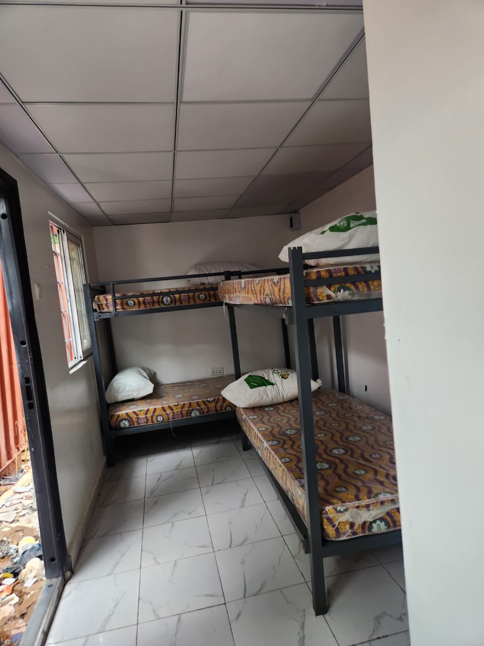 Finished container room interior with bunk beds, tiled floor and ceiling grid